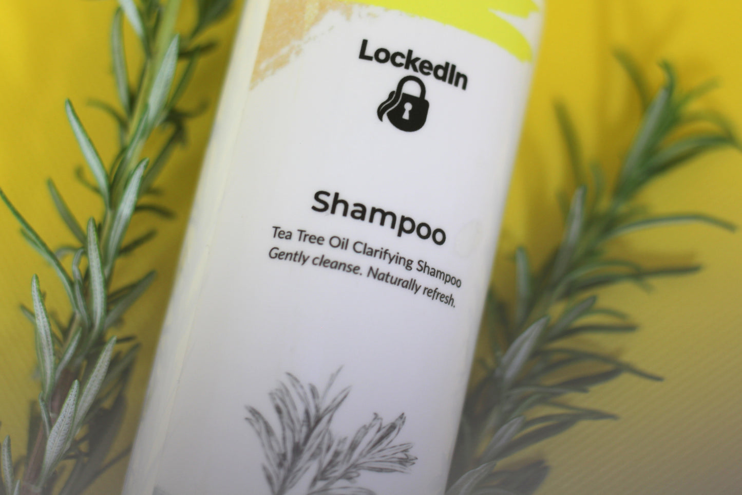 Shampoo bottle labeled 'LockedIn' with tea tree oil text, surrounded by rosemary leaves on a yellow background